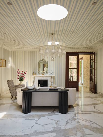 The salon, or formal living room, is a stage set for conversations. Sunlight from twin skylights casts drama across striped walls, a restored fireplace, and a mix of sculptural and classic furniture.