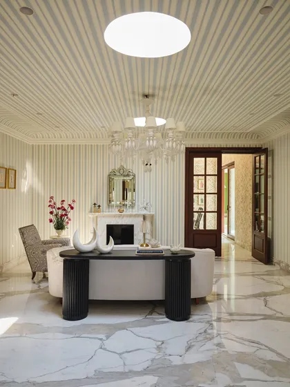The salon, or formal living room, is a stage set for conversations. Sunlight from twin skylights casts drama across striped walls, a restored fireplace, and a mix of sculptural and classic furniture.