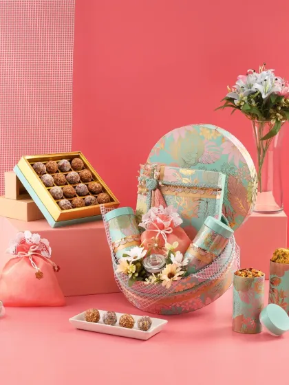 A stunning festive hamper arrangement in a pastel teal and pink color palette. Featuring a round box, a mesh basket, and a box of gourmet sweets, this showcases our ability to create visually striking and luxurious gift sets.