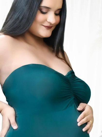 A simple and beautiful close-up of an expectant mother cradling her bump. The focus is on her connection with her baby, highlighted by the elegant green dress.