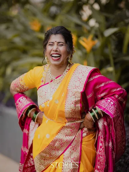 The purest expression of joy. A Maharashtrian bride in a bright yellow and pink saree bursts into laughter, a candid moment that perfectly captures the happiness of her wedding day.