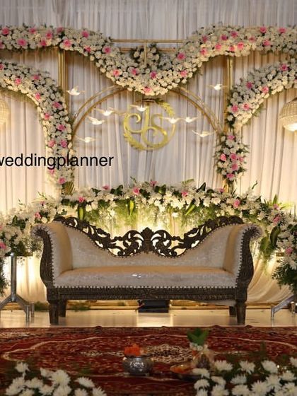 A sophisticated engagement stage with golden arches draped in white and pink flowers, a custom monogram of the couple's initials, and elegant seating.