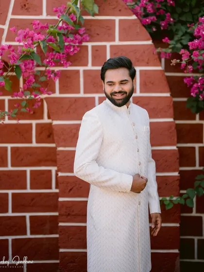 A candid portrait of the groom, Shantanu, smiling against a backdrop of brick and bougainvillea.