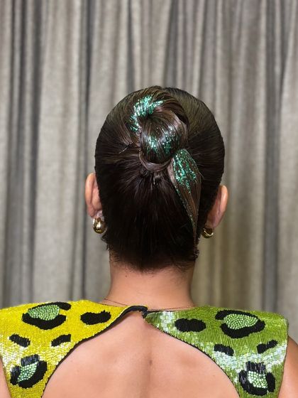 For a modern party look, a touch of glitter can transform a simple bun. This image showcases a sleek, high bun with a green glitter accent, a fun technique I cover for creating eye-catching cocktail hairstyles.