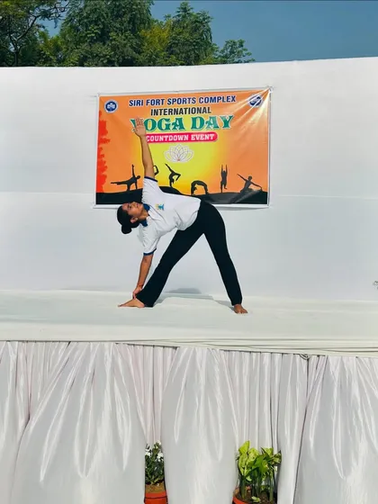 Performing Trikonasana (Triangle Pose) on stage at the Siri Fort Sports Complex for an International Yoga Day countdown event. This pose is excellent for stretching the entire body.