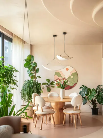 The round dining table and curved chairs continue the home's organic theme. A circular art piece on the wall adds a pop of color that complements the surrounding greenery and earthy tones.