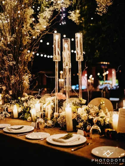 A dream dinner setting. The long table is adorned with a runner of white and pink florals and dozens of candles, creating an intimate and romantic glow under a canopy of fairy lights.