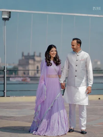 A full-length shot of the couple during their outdoor engagement session. The bride's lavender lehenga looks stunning against the bright blue sky.