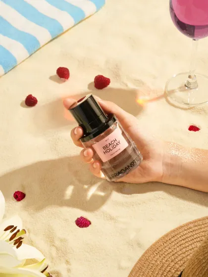A lifestyle beach scene created in our studio with sand, a beach towel, and a hand model holding the perfume. We can create any environment to tell your product's story.