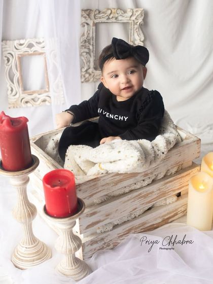 Dressed in style and glowing with charm. This cozy studio setup with a rustic crate, soft blanket, and warm candlelight creates a sophisticated and sweet portrait.