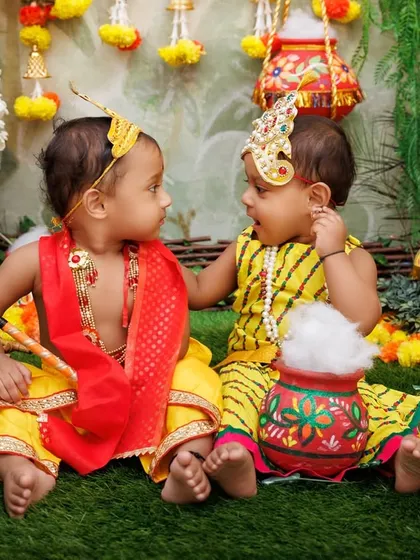 A precious moment between two babies dressed as Krishna and Radha, sharing a secret.