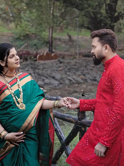 A classic couple's portrait from a traditional maternity session. The contrast of her green saree and his vibrant red kurta makes for a visually striking image, celebrating their journey together.