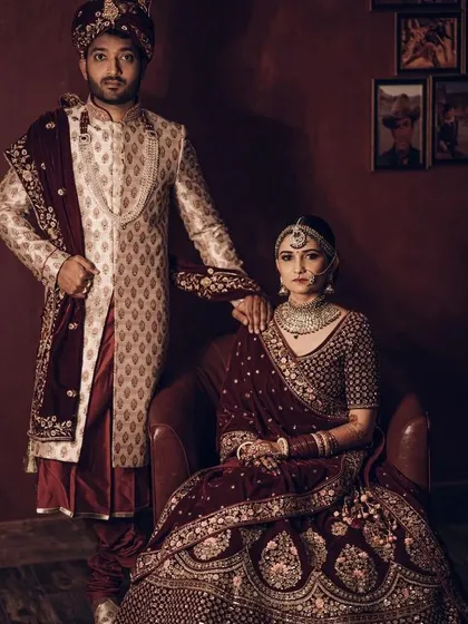 This is one of our classic bridal couple sets, perfect for the main wedding ceremony. The bride is wearing a deep maroon velvet lehenga with detailed zardozi work, and the groom is in a cream and gold patterned sherwani with a matching maroon stole. We help you get this complete, perfectly coordinated look without the stress.