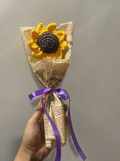A single crochet sunflower wrapped in newspaper with a purple ribbon. This is one of my best-selling items for a reason.