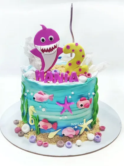 A vibrant Baby Shark theme cake perfect for a second birthday. The underwater scene is created with buttercream waves and edible sea creatures, all surrounding a fun, pink shark topper.
