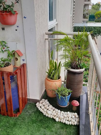 This is a simple yet effective balcony corner. I used a wooden crate to cleverly hide a water can, placed a birdhouse on top, and arranged a few large planters to create a green and functional space.