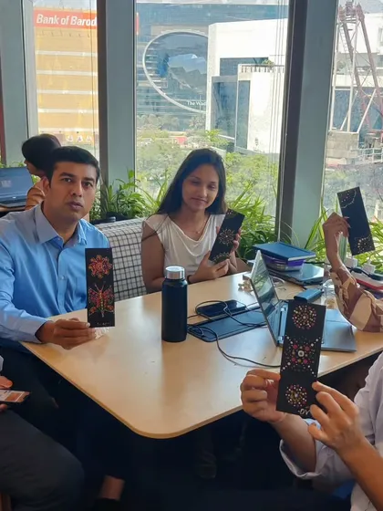 A group of colleagues from Colliers proudly display the dot art bookmarks they made during a corporate workshop. The office setting with a city view in the background highlights the convenience of on-site creative sessions.