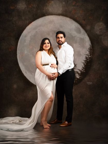 A magical couple portrait set against a full moon backdrop. The coordinated white outfits and water reflection effect create a dreamy and romantic scene.