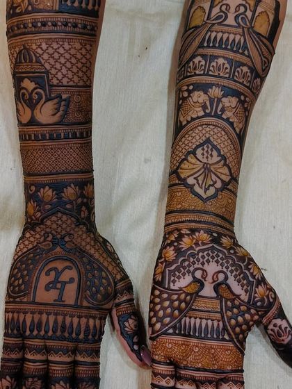 A closer look at a custom design featuring the couple's initials 'H' and 'T'. The arms are adorned with swans, elephants, and palace architecture.