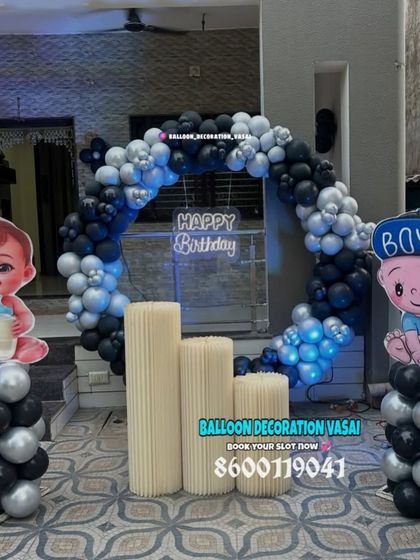 A simple and cute "Baby Boy" themed decoration. This outdoor setup features a black and silver balloon ring, character cutouts, and plinths for the cake.