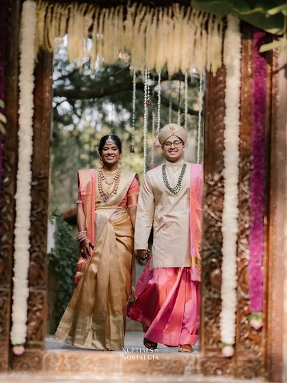 A grand entrance through a beautifully decorated doorway. The couple is framed by traditional floral hangings, creating a picture-perfect wedding shot.