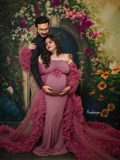 A romantic couple's portrait against a floral arch. The rich color of her ruffled gown and his dark shirt create a beautiful contrast.
