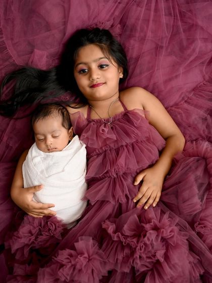 A beautiful overhead shot of a big sister holding her newborn brother. The rich color of their matching outfits and the peaceful look on their faces make this a truly special sibling portrait.