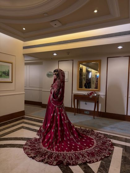 A full-length photo of Iffat in her stunning red bridal gown. The long train and intricate embroidery create a look of pure royalty.