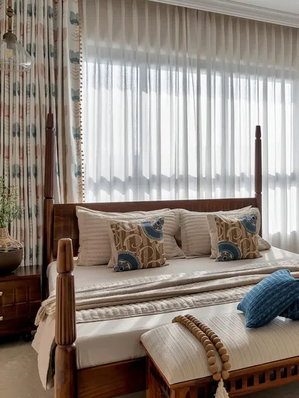 A classic four-poster bed brings a sense of timeless elegance to this room. The space is kept light and airy with sheer curtains and a neutral color palette accented with blue.