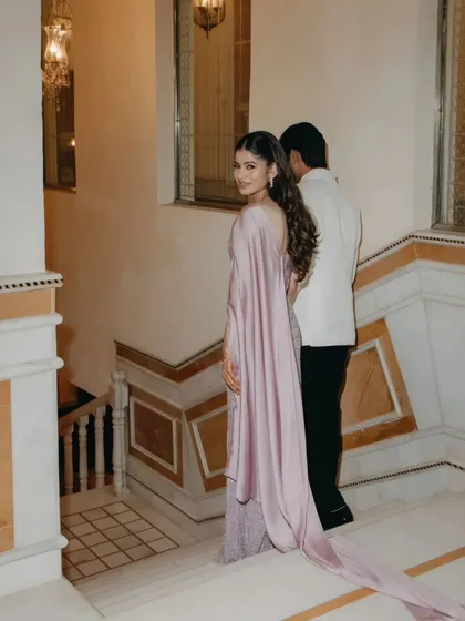 The bride looks back with a smile as she and the groom walk down a marble staircase, her flowing gown adding a touch of drama.