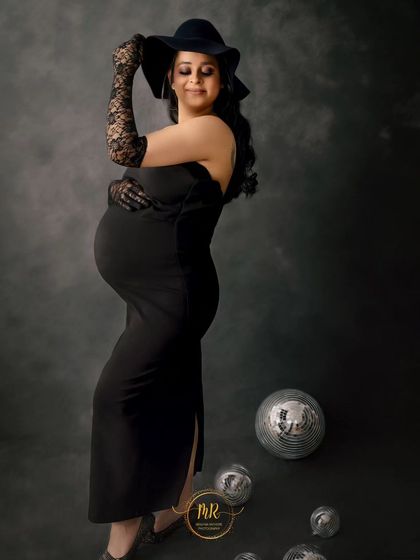 A full-length view of a modern maternity look. The black dress, hat, and gloves create a sophisticated silhouette, perfect for a fashion-forward photoshoot.