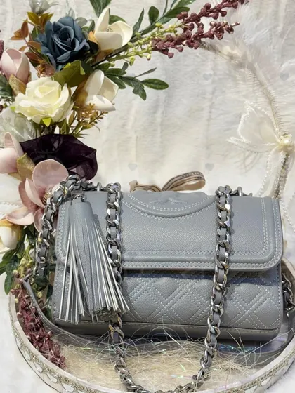 A stylish grey handbag with a silver chain, placed on a decorative tray. The floral arrangement in shades of blue, white, and mauve complements the bag perfectly, creating a cohesive and beautiful gift.