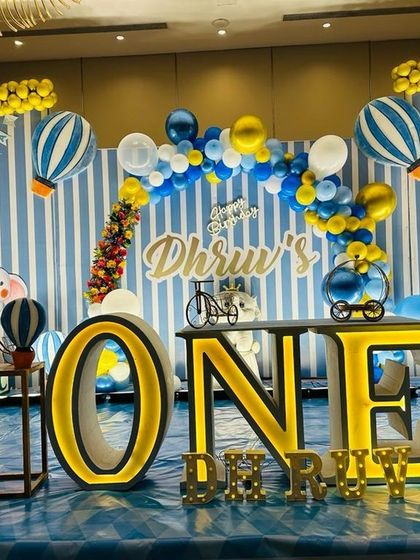 This 'Up and Away' theme features hot air balloon props, a striped blue and white backdrop, and large illuminated 'ONE' letters for a first birthday.