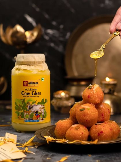 A spoonful of golden ghee is drizzled over a stack of Motichoor Ladoos. The scene is set with diyas and brass plates, creating a warm, festive atmosphere perfect for Diwali.