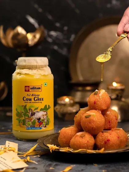 A spoonful of golden ghee is drizzled over a stack of Motichoor Ladoos. The scene is set with diyas and brass plates, creating a warm, festive atmosphere perfect for Diwali.