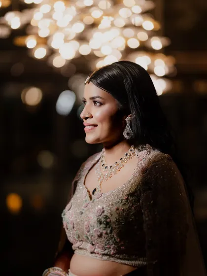 A lovely portrait of the bride at her Sangeet, with the warm glow of decorative lights creating a beautiful bokeh effect. Her elegant jewelry and happy expression shine through.