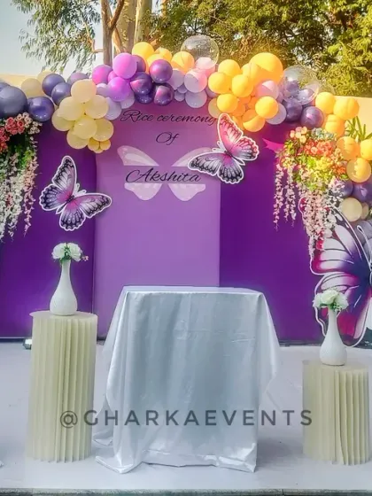 The main stage for the butterfly-themed Rice Ceremony. The purple backdrop is adorned with large butterfly cutouts and a beautiful balloon arrangement, creating a magical setting.