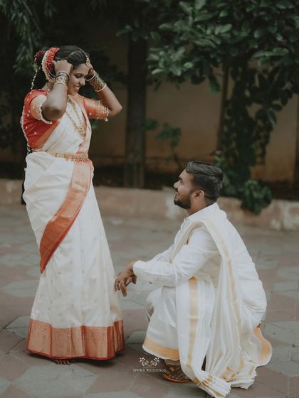 A playful and loving moment as the groom kneels before his bride, who is adjusting her hair with a smile.