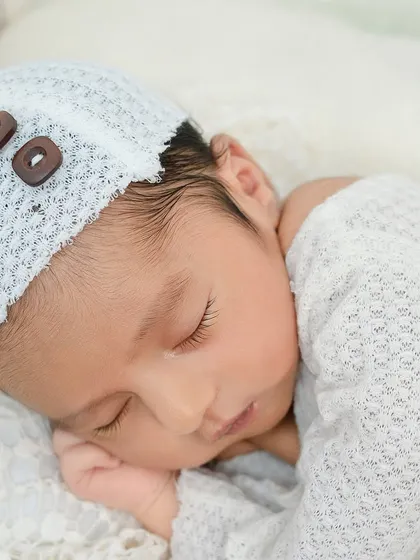 A close-up of a sleeping newborn's face, showcasing the delicate texture of their hair and the soft knit of their bonnet. These are the quiet, beautiful moments I love to capture.