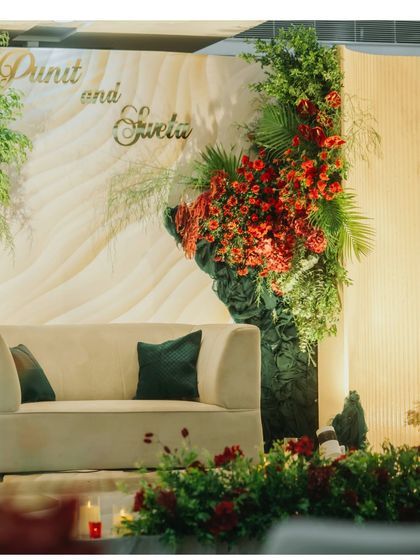 A modern reception stage with a unique floral installation of red and green. The elegant cream backdrop and custom name sign add a signature touch to the couple's celebration.