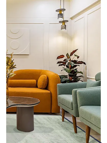 A cozy corner featuring a mustard sofa and soft green armchairs. The combination of warm and cool tones, along with lush plants, creates a balanced and inviting atmosphere.