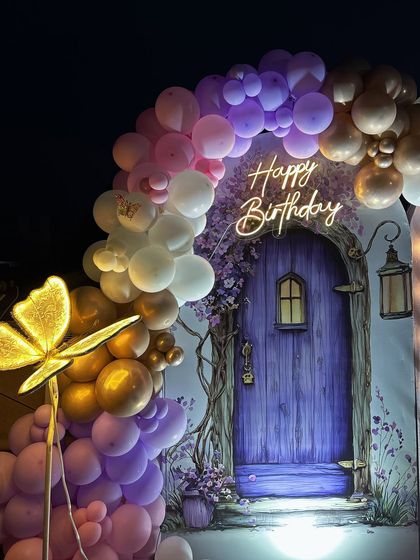 A closer look at the enchanting details, featuring a beautiful balloon arch in shades of purple, pink, and gold, framing the custom 'Happy Birthday' neon sign and fairy door backdrop.