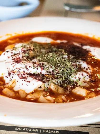 A comforting bowl of Turkish Manti (dumplings) in a yogurt and tomato sauce. The shot captures the rustic, hearty nature of the dish.