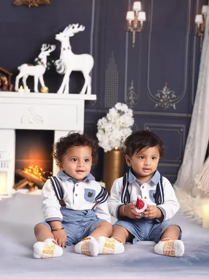 Double the joy! These adorable twins are dressed in matching outfits, ready to celebrate their first Christmas together.
