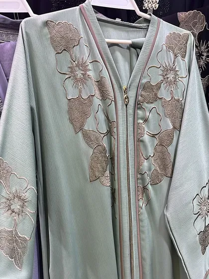 A lovely mint green abaya with large, embroidered floral patterns. The zip front and wide sleeves make it both stylish and comfortable.