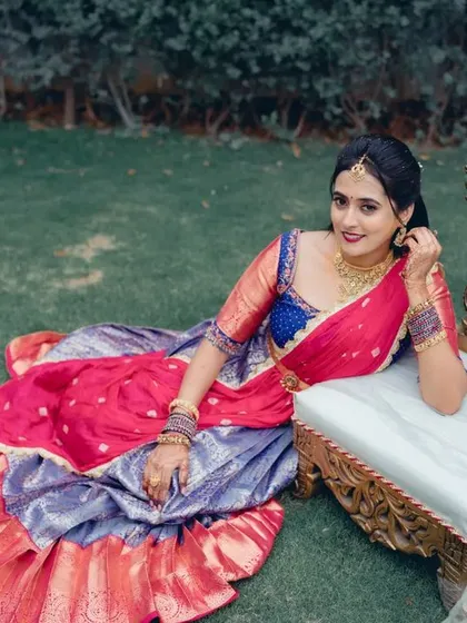 A regal portrait of the bride in a vibrant half saree, seated on an ornate chair. This outdoor shot has a royal and traditional feel.