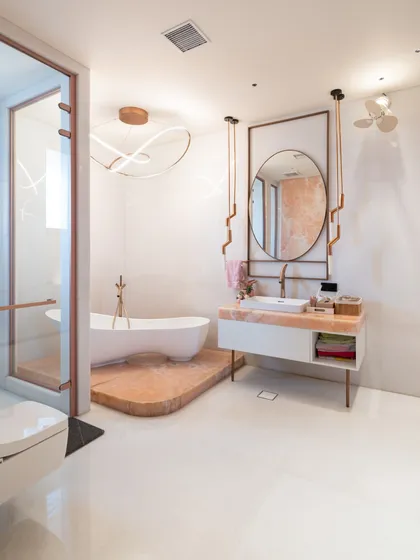 Luxury extends to every corner of the home. In this bathroom for Residence 100, a freestanding tub sits on a raised marble platform, complemented by rose gold fixtures and custom lighting for a spa-like retreat.
