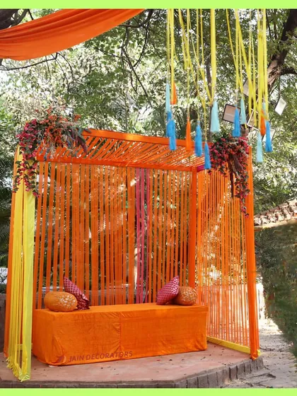 A simple and bright seating area for a Haldi ceremony. The orange-draped structure is perfect for a sunny, outdoor event.