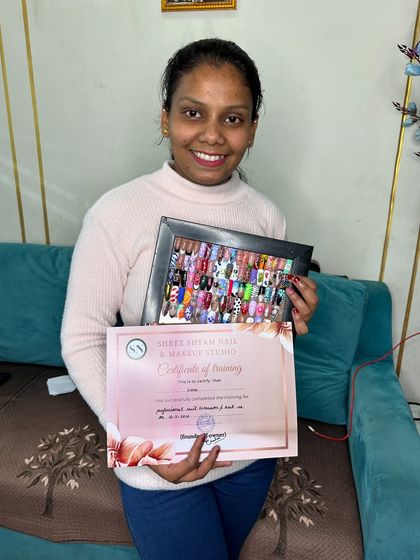 This is what success looks like. A happy student holding her hard-earned certificate and her portfolio showcasing over 26 different nail art styles.