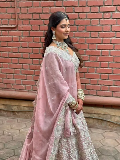 A side view against a brick wall, showing the beautiful contrast between the soft pastel outfit and the rustic background. Her makeup remains flawless and glowing.